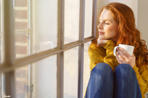 Woman holding cup of coffee looking out a window
